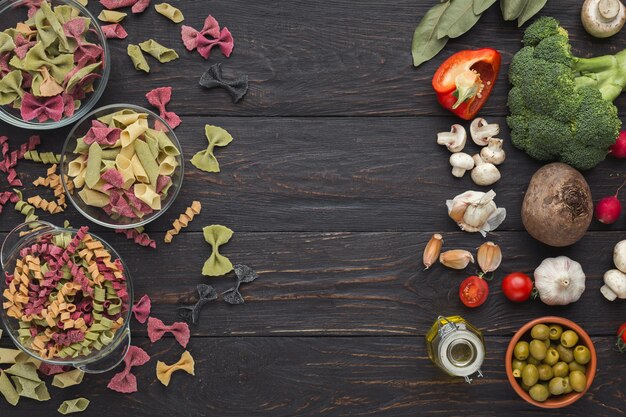 Foto conceito de comida italiana. vários tipos de massas coloridas em tigelas. vista superior sobre fundo escuro de madeira rústica. copie o espaço para a receita