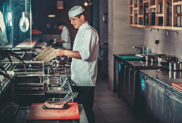 Conceito de comida jovem chef bonito em uniforme branco acende brasas e monitora o grau de temperatura para