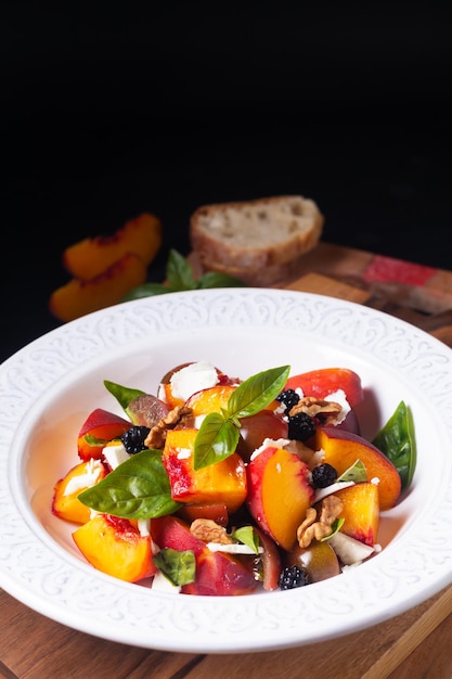 Conceito de comida saudável Salada de tomate e pêssego com manjericão e queijo de cabra na placa de madeira em fundo preto com espaço de cópia