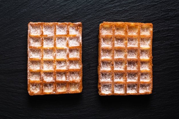 Conceito de comida Waffles quadrados clássicos com suging de confeiteiro toping na placa de pedra ardósia preta