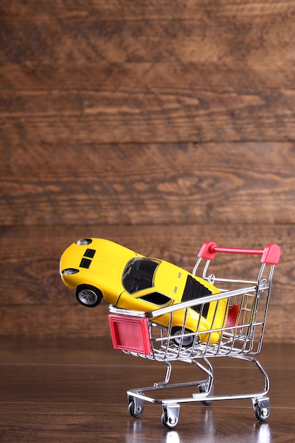 Conceito de compra de um carro novo. carro de brinquedo no carrinho de compras na mesa de madeira