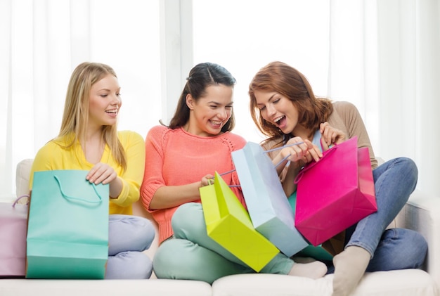 Conceito de compras e estilo de vida - três adolescentes sorridentes com muitas sacolas de compras em casa