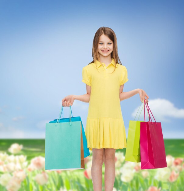 conceito de compras, felicidade e pessoas - sorridente menina de vestido amarelo com sacolas de compras