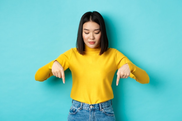 Conceito de compras. jovem adolescente coreana apontando e olhando para um comercial, em pé contra um fundo azul