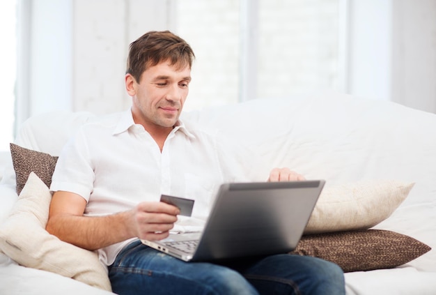 conceito de compras online ou pela internet - homem sorridente com laptop e cartão de crédito em casa