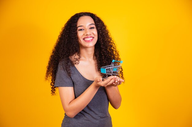 Conceito de compras. retrato de uma mulher sorridente segurando um carrinho de compras vazio na palma da mão, isolado em um fundo amarelo