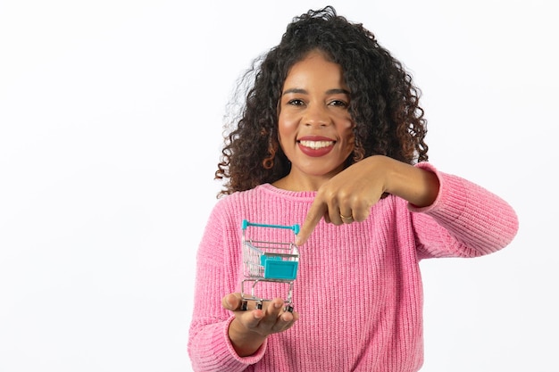 Conceito de compras Retrato de uma mulher sorridente segurando um pequeno carrinho de compras vazio na palma da mão isolada