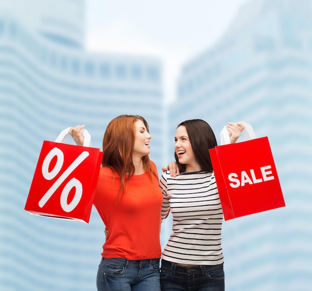 conceito de compras, venda e presente - duas adolescentes sorridentes com sacolas de compras e sinal de porcentagem ao ar livre