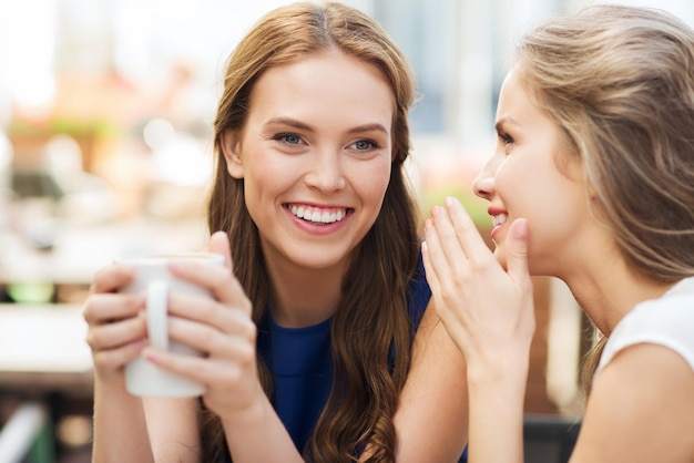 Conceito de comunicação e amizade de pessoas - mulheres jovens sorridentes bebendo café ou chá e fofocando no café ao ar livre