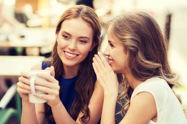 conceito de comunicação e amizade de pessoas - mulheres jovens sorridentes bebendo café ou chá e fofocando no café ao ar livre