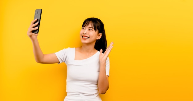 Conceito de comunicação online aprendizagem online Retrato de menina asiática fofo feliz em vestido branco falando no celular e rindo em um fundo amarelo
