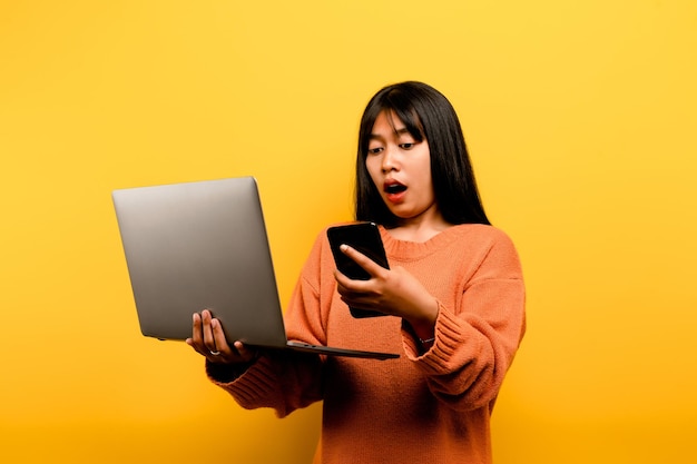 Conceito de comunicação online menina asiática usa laptop em casa foto de estúdio amarelo ela está feliz em passar seu tempo livre online enquanto conversa com amigos nas redes sociais fazendo compras ou trabalhando online