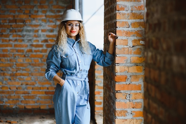 Conceito de construção. Construtor muito feminino de macacão e capacete trabalhando no canteiro de obras.