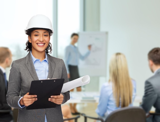 conceito de construção, desenvolvimento, construção e arquitetura - empresária sorridente no capacete branco com prancheta e planta no escritório