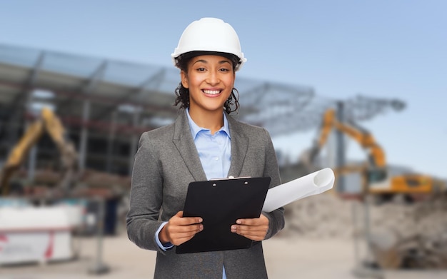 conceito de construção, desenvolvimento, construção e arquitetura - mulher sorridente no capacete branco com planta e prancheta