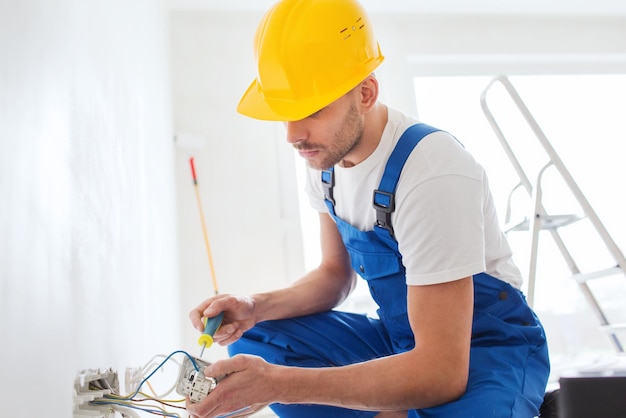 conceito de construção, renovação, tecnologia, eletricidade e pessoas - construtor com soquete de fixação de chave de fenda dentro de casa