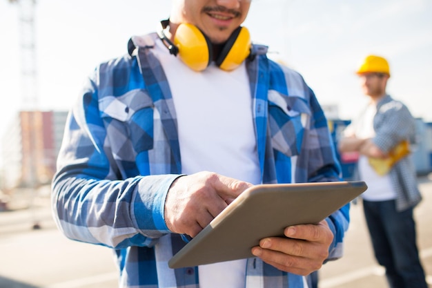 conceito de construção, tecnologia e pessoas - close-up do construtor sorridente com fones de ouvido e computador tablet pc ao ar livre