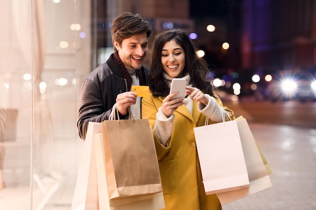 Conceito de consumismo Casal feliz verificando o celular ao ar livre