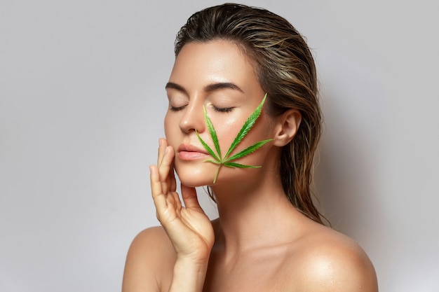 Conceito de cosméticos CBD. Mulher bonita com uma folha de cannabis em fundo cinza