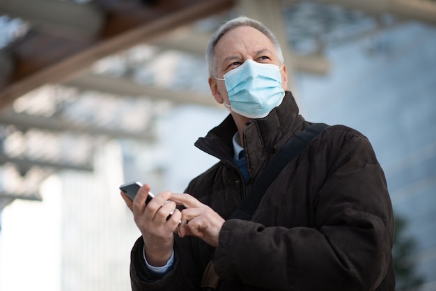 Conceito de covid coronavirus, homem de negócios idoso mascarado usando seu smartphone ao ar livre