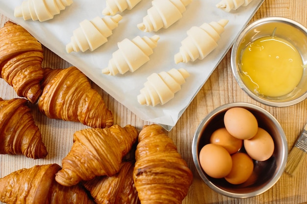 Conceito de cozimento de croissant croissants crus enrolados e recém-assados, bem como ingredientes, estão sobre a mesa