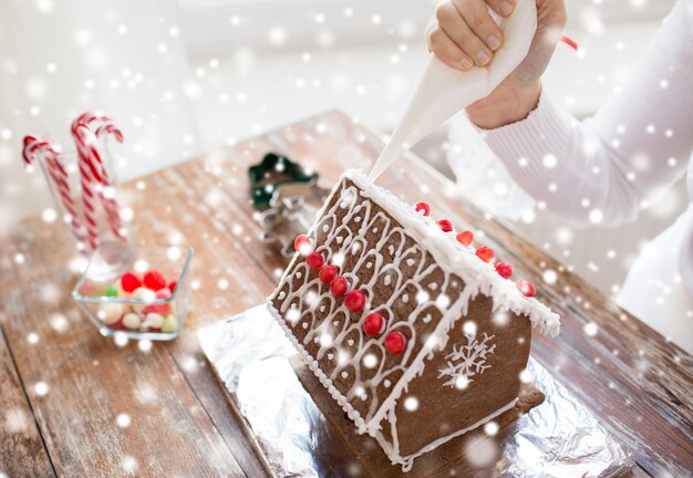 Conceito de cozinha, pessoas, natal e decoração - close-up de uma mulher feliz fazendo casas de gengibre em casa