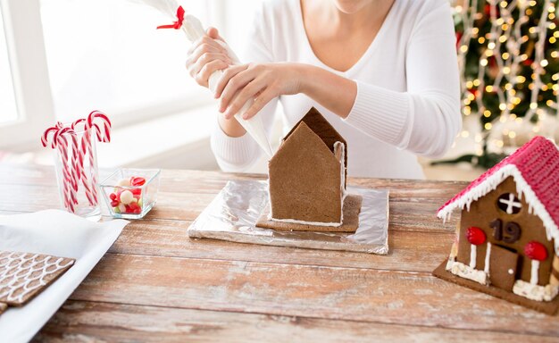 conceito de cozinha, pessoas, natal e decoração - mulher feliz fazendo casas de gengibre em casa