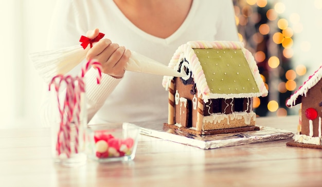 Foto conceito de cozinha, pessoas, natal e decoração - mulher feliz fazendo casas de gengibre em casa