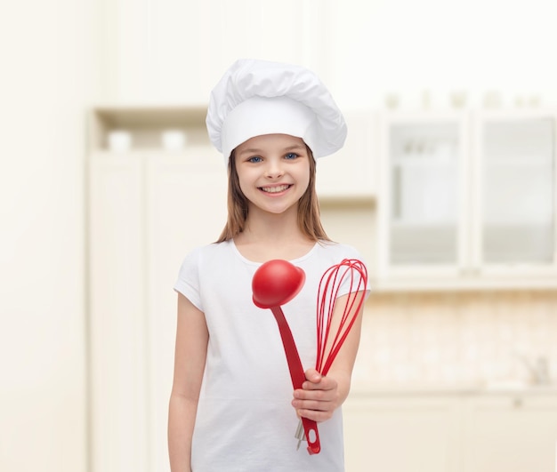 conceito de cozinhar e pessoas - menina sorridente no chapéu de cozinheiro com concha e batedor