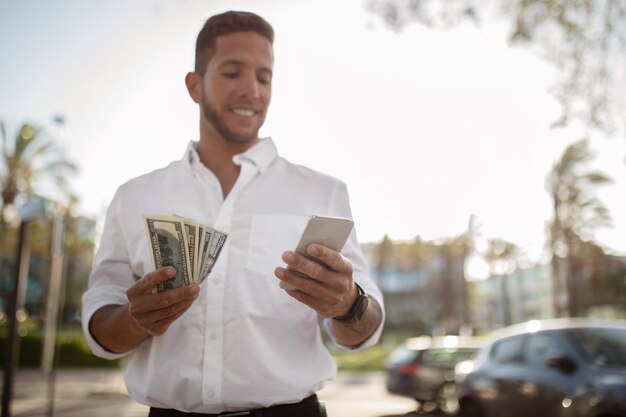 Foto conceito de crédito bancário on-line feliz jovem empresário com notas de dólar e realização de telefone