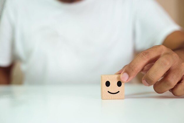 Foto conceito de crescimento sucesso mão segurando cubo de bloco de madeira com rosto sorriso símbolo de emoção satisfação e classificação de serviço