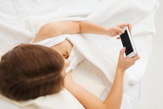 conceito de criança, tecnologia e internet - menina deitada na cama com smartphone em casa