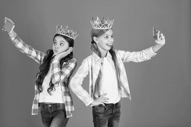 Conceito de crianças mimadas Princesa egocêntrica Crianças usam coroas douradas símbolo princesa Sinais de alerta de criança mimada Evite criar crianças mimadas Meninas tirando selfie câmera de smartphone