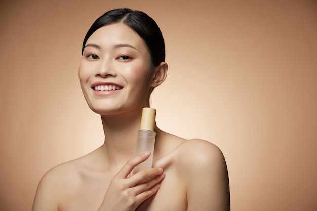Conceito de cuidados com a pele - jovem e encantadora mulher asiática segurando frasco spray e loção com composição de foto de maquiagem perfeita de menina morena