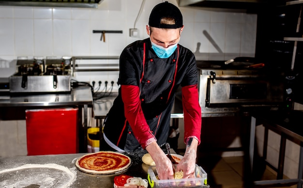 Conceito de culinária de pizza, chef com máscara médica colocando pasta de tamat na pizza