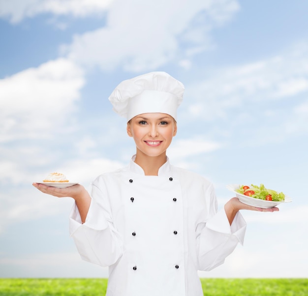 Conceito de culinária e comida - chef feminino sorridente, cozinheiro ou padeiro com salada e bolo em pratos