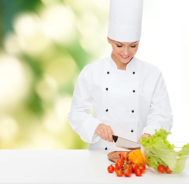 conceito de culinária e comida - sorridente chef feminina cortando legumes