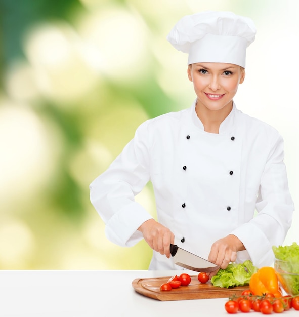 conceito de culinária e comida - sorridente chef feminina, cozinheira ou padeiro cortando legumes