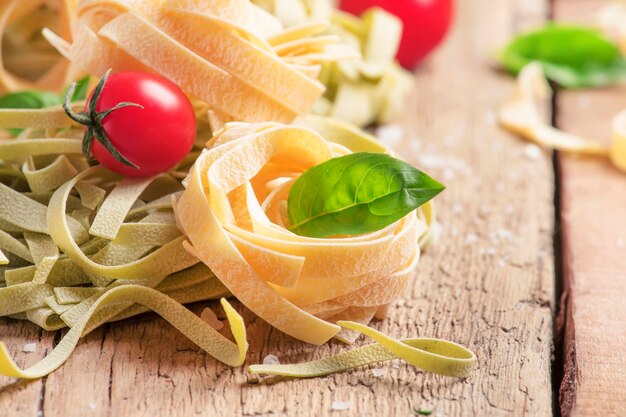 Conceito de culinária italiana com macarrão tagliatelle verde e amarelo tomate cereja vermelho e manjericão verde mesa de cozinha de madeira rústica foco seletivo