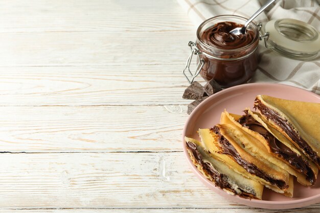 Conceito de delicioso café da manhã com crepes com pasta de chocolate em fundo branco de madeira