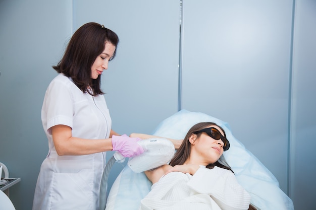 Foto conceito de depilação a laser, fotoepilação, corpo e cuidados com a pele. jovem mulher remove o cabelo das axilas na clínica de cosmetologia. close up, conceito de procedimento de higiene