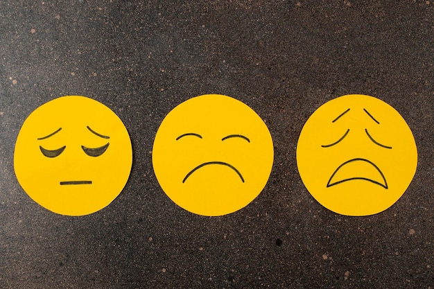 Conceito de depressão Doença psicológicaxA Três emoticons tristes em um fundo escuro visto de cima