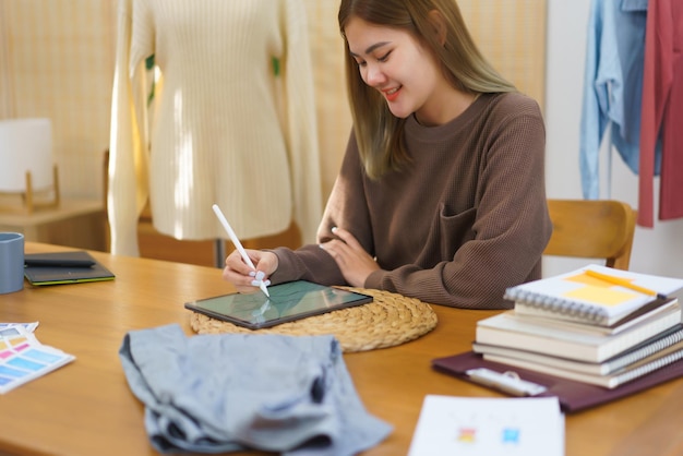 Conceito de design de moda Desenhista de moda esboçando novas roupas de coleção em tablet em seu escritório em casa