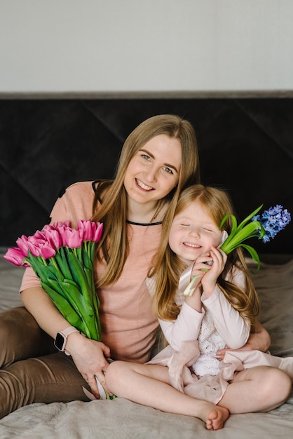 Conceito de dia das mães Menina bonitinha cumprimentando a mãe e dá a ela um buquê de flores tulipas em casa Mãe e filha sorrindo e abraçando Feliz feriado em família e união