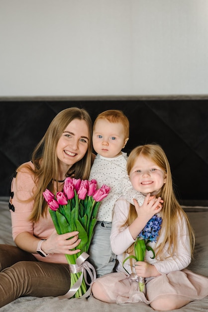 Conceito de dia das mães Menina bonitinha e menino cumprimentando a mãe e dá a ela um buquê de flores tulipas em casa Mãe e filha filho sorrindo e abraçando Feliz feriado em família e união