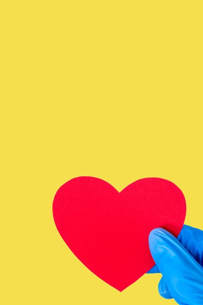 Conceito de dia dos namorados 2021. Mão com luvas médicas azuis e segurando um coração vermelho