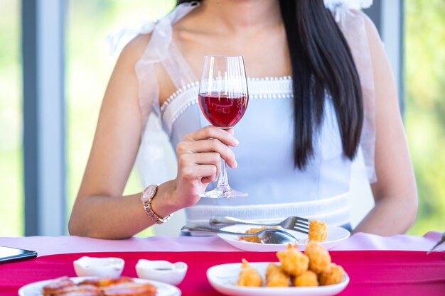 Conceito de dia dos namorados, jovem asiática sentada à mesa de comida com taças de vinho e buquê de vinho de rosas vermelhas e rosa e esperando por seu homem no fundo do restaurante