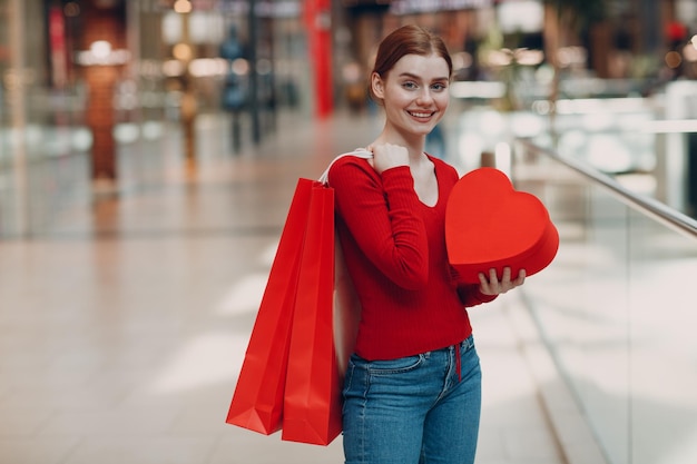 Conceito de Dia dos Namorados Jovem com sacolas de compras e retrato de caixa em forma de coração vermelho na loja do shopping