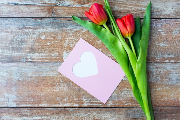 conceito de dia dos namorados, saudação, amor e feriados - close-up de tulipas vermelhas e cartão com coração