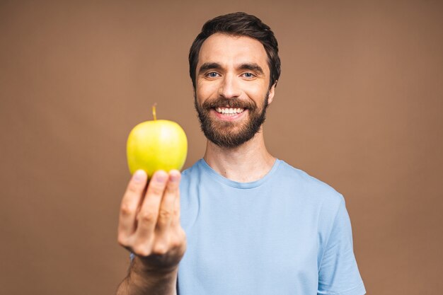 Conceito de dieta. Alegre linda barbudo jovem comendo maçã verde, isolada sobre fundo bege.